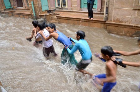 Photo for Boys playing flowing water of monsoon on road Jodhpur India - Royalty Free Image