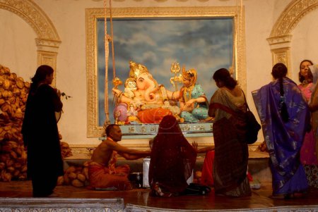 Photo for Idol of Lord Ganesh sitting on Swing as Lord Vishnu with Laxmi with Pujari and worshiper ; Elephant Headed God of Hindu worshiping for Ganapati Festival at Mandai ; Pune ; Maharashtra ; India ; Asia - Royalty Free Image