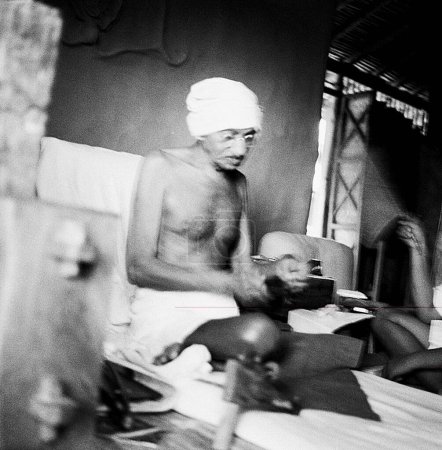 Foto de Mahatma Gandhi girando sobre el instrumento de Dhanush Takli en su cabaña en el Ashram Sevagram, 1940 - Imagen libre de derechos