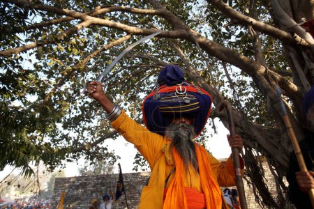 Téléchargez les photos : Guerrier nihang ou sikh en pagdi ou coiffure portant épée et bâton de bois lors des célébrations de Hola Mohalla à Anandpur sahib dans le district de Rupnagar ; Punjab ; Inde - en image libre de droit