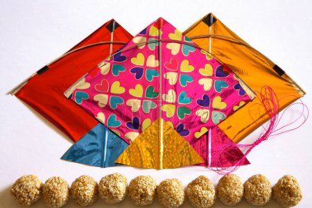 Colourful kites thread and sweet tilgur or til gul sesame laddoos for Makara Sankranti festival on white background