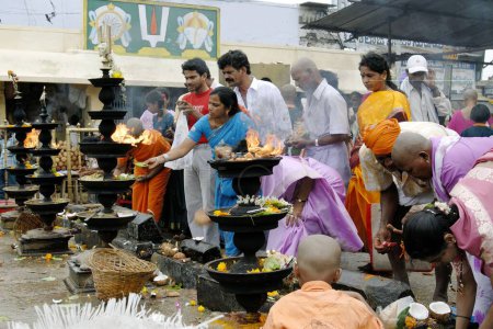 Foto de Devotos adorando y ofreciendo coco, alcanfor y flores al Señor Venkateshwara, Balaji frente a las enormes lámparas de aceite en el templo Tirumala, Tirupati, Andhra Pradesh, India - Imagen libre de derechos