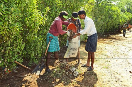 Téléchargez les photos : Bénévoles de l'ONG Chinmaya Organization of Rural Development CORD utilisant la pelle pour nettoyer la route du village dans le cadre de la collecte de propreté, Siruvani, Karnataka, Inde - en image libre de droit