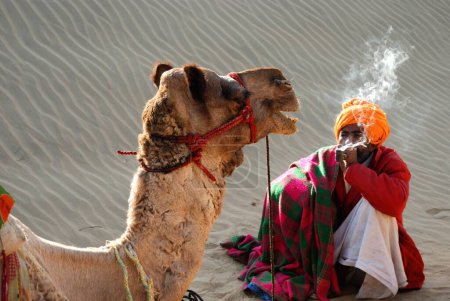 Foto de Camello y hombre fumando en el desierto en Khuri Khuhri, Jaisalmer, Rajastán, India - Imagen libre de derechos