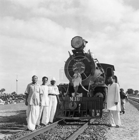 Foto de Cuatro hombres de pie frente al tren especial Gandhiji en Madras, 1946 El conductor del tren estaba tan entusiasmado con Gandhi que puso su fotografía de tamaño natural delante del motor - Imagen libre de derechos