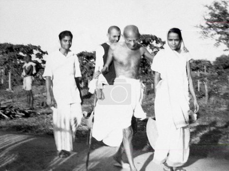 Photo for Mahatma Gandhi walking with Shailendra Chatterjee, Chimanlalbhai Shah managing trustee of Sevagram Ashram and Prabhavatibehn Jayaprakash at Sevagram Ashram, 1941 - Royalty Free Image