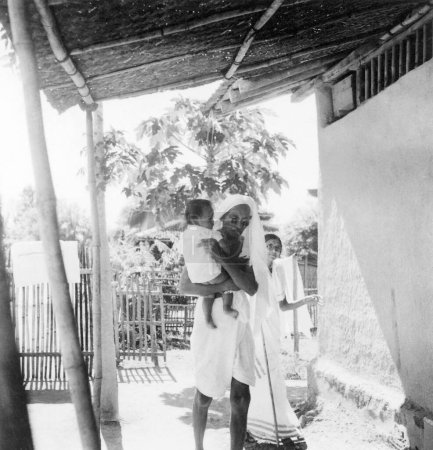 Foto de Mahatma Gandhi, llevando a Anand, hijo de Shardabehn Shukawala en el Ashram Sevagram, 1940 - Imagen libre de derechos