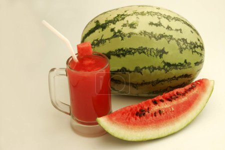 Fruits ; One full watermelon with light and dark green stripes with glass of melon juice and cut slice showing red watery pulp and black seeds ; Pune; Maharashtra ; India