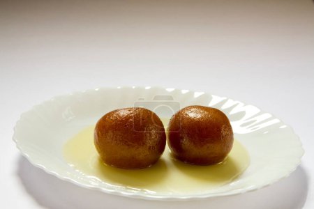 Téléchargez les photos : Nourriture sucrée indienne double paire deux morceaux de forme ronde Gulabjamun Bonbon Confiserie avec sirop de sucre servi dans une assiette - en image libre de droit