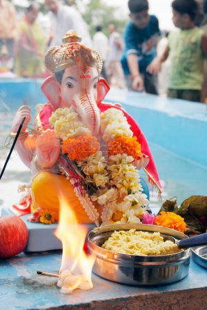 Small idol of lord ganesh elephant headed god ready to immersed with small fire and sweet offering in front of it ; Pune ; Maharashtra ; India