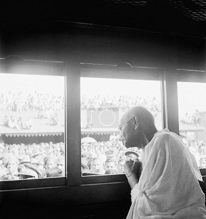 Téléchargez les photos : Mahatma Gandhi, regardant par la fenêtre d'un train vers le public dans une gare, 1940 - en image libre de droit