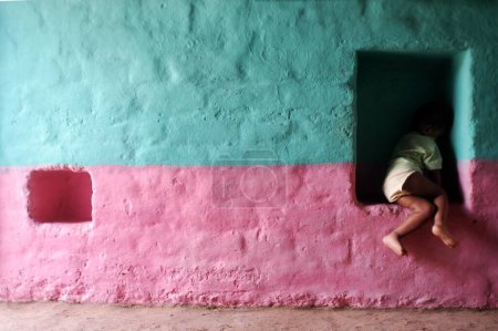 Foto de Un niño sentado en la pared santificaciones hechas para mantener las cosas en las casas de barro de Hasur Champu aldea en el distrito de Gadhinglaj de Maharashtra; India - Imagen libre de derechos