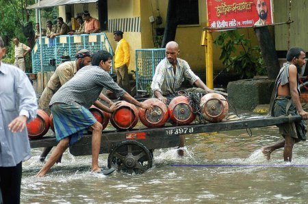 Téléchargez les photos : Les travailleurs transportent des bouteilles de gaz GPL sur un chariot dans l'eau inondée causée par de fortes pluies à Bombay Mumbai ; Maharashtra ; Inde - en image libre de droit