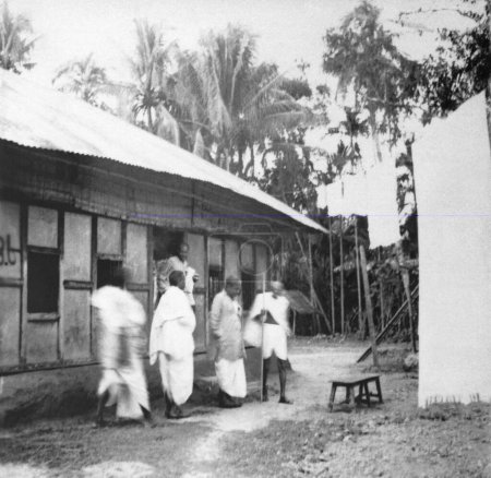 Foto de Mahatma Gandhi y otros en frente de una casa en un pueblo afectado por disturbios en Noakhali Bengala Oriental; Noviembre 1946; India - Imagen libre de derechos