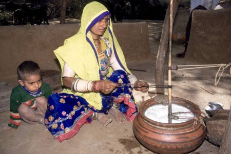 Téléchargez les photos : Femme Rajasthan baratter caillé dans pot d'argile enfant assis près d'elle ; Jodhpur ; Rajasthan ; Inde - en image libre de droit