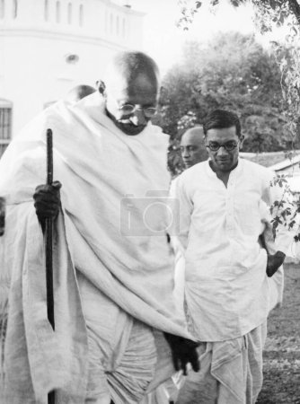 Téléchargez les photos : Mahatma Gandhi et Dewadarji Damodar Mundada marchant à l'ashram de Sevagram, 1939, moitié couvert Sardar Vallabhbhai Patel - en image libre de droit