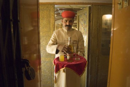 Téléchargez les photos : Rajasthani agent tenant plateau de bière dans le patrimoine sur roues Voyage dans le train touristique de luxe passé ; Rajasthan ; Inde - en image libre de droit