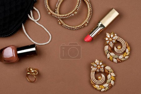 Téléchargez les photos : Bijoux de perles sur fond brun, rouge à lèvres, bracelet de perles, vernis à ongles, collier de perles, boucles d'oreilles en perles, bague de doigt. Style, mode et design de bijoux. bijoux traditionnels indiens, backgroud bijoux - en image libre de droit