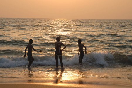 Téléchargez les photos : Enfants jouant avec les vagues de la mer ; coucher de soleil sur la plage de Sagreshwar ; Vengurle ; district de Sindhudurg ; Maharashtra ; Inde - en image libre de droit