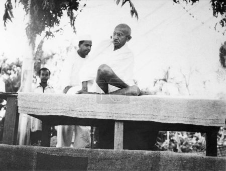 Foto de Mahatma Gandhi sentado en el estrado después de los disturbios entre hindúes y musulmanes en Noakhali Bengala Oriental, noviembre 1946 - Imagen libre de derechos