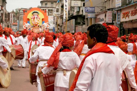 Foto de Chicas y hombres indios que usan sombreros de color rojo llamados pijamas feta y kurta blancos y que tocan un instrumento musical llamado dhol durante el festival de inmersión del señor Ganesh ganpati elefante cabeza dios, Pune; Maharashtra, India - Imagen libre de derechos