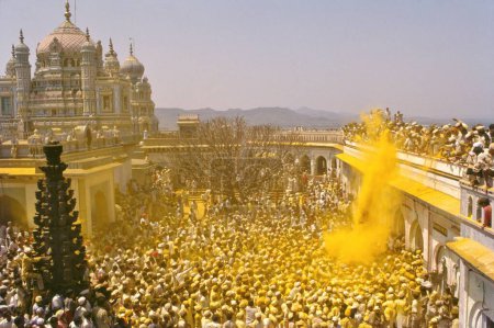 Foto de El palanquín que lleva las imágenes de Khandoba y Malshabai sale de la puerta del templo, la multitud explota en consignas rituales, cubriendo a todos en el parentesco amarillo de la devoción, Jejuri, Maharashtra, India - Imagen libre de derechos