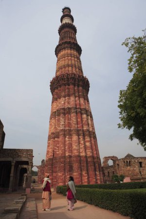 Téléchargez les photos : Sadhu indien observant Qutb Minar construit en 1311 tour de grès rouge, art indo-musulman, sultanat de Delhi, Delhi, Inde Site du patrimoine mondial de l'UNESCO - en image libre de droit