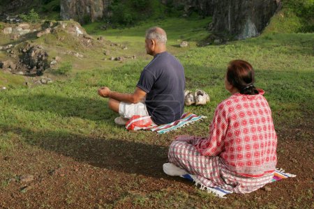 Téléchargez les photos : Couple d'âge moyen assis dans un champ vert frais ouvert le matin et faisant de l'exercice respiratoire appelé Pranayam, Inde - en image libre de droit