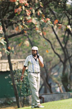 Foto de El jugador de críquet indio de Asia del Sur y ex capitán de críquet indio Kapil Dev hablando por teléfono celular y jugando al golf en Bombay Presidency Golf Club (BPGC) en Chembur; Bombay Mumbai; Maharashtra; India - Imagen libre de derechos
