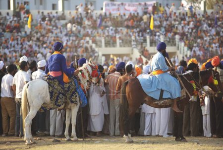 Téléchargez les photos : Les gens regardent les cascades de Nihangs ou guerrier sikh, lors d'événements culturels pour les célébrations du 300e anniversaire de la consécration du perpétuel Sikh Guru Granth Sahib au terrain de sport Khalsa, Nanded, Maharashtra, Inde - en image libre de droit