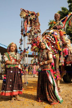 Photo for Girls in traditional jewellery and rajasthani costume standing in front of decorated camel in Pushkar fair, Rajasthan, India - Royalty Free Image