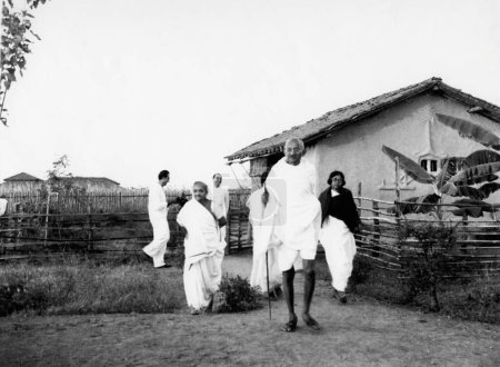 Téléchargez les photos : Kasturba Gandhi, Mahatma Gandhi, ashramite Shardabehn Shukawala marchant devant la cabane Mahatma Gandhis à l'Ashram de Sevagram, 1939 - en image libre de droit