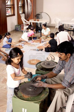 Foto de Clase de cerámica para niños, alfarero enseñando a los niños cómo hacer olla en la rueda con otras técnicas - Imagen libre de derechos