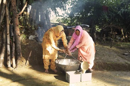Foto de Mujeres rurales vertiendo ingredientes hirvientes en moldes metálicos haciendo jabón de lavado iniciativa económica iniciada por la ONG Chinmaya Organización de Desarrollo Rural CORD, Sidhbari, Himachal Pradesh, India - Imagen libre de derechos