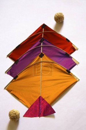 Colourful kites and sweet tilgur or til gul sesame laddoos for Makara Sankranti festival on white background