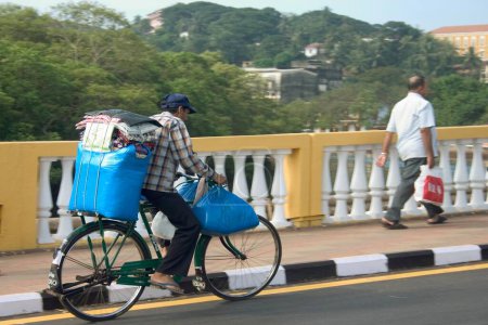 Foto de Equipaje azul transportado en bicicleta sobre el puente Old Pato, puente amarillo sobre el río Mandovi, Mahatma Gandhi Road, Panjim, Goa, India - Imagen libre de derechos