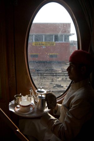 Téléchargez les photos : Rajasthani préposé tenant plateau de boisson debout à l'extérieur du patrimoine sur roues Voyage dans le train touristique de luxe passé ; Rajasthan ; Inde - en image libre de droit