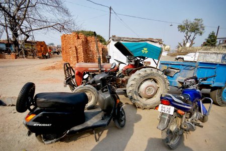 Foto de Un scooter; motocicleta y un tractor estacionados en el lado de la carretera, Dehradun, Uttaranchal, India - Imagen libre de derechos