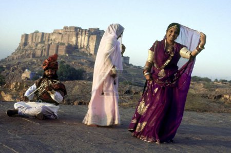 Téléchargez les photos : Danses folkloriques, femmes rajasthanes dansant et homme jouant de l'instrument de musique mehrangarh fort en arrière-plan, Jodhpur, Rajasthan, Inde - en image libre de droit