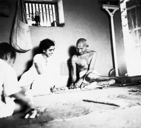 Téléchargez les photos : Mahatma Gandhi assis avec Sushila Nayar et d'autres dans sa cabane à l'ashram de Sevagram, 1937 - en image libre de droit