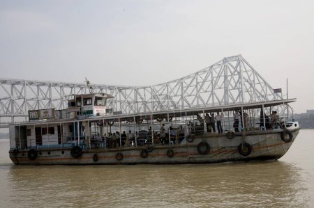 Photo for Ferry in water and Howrah bridge now Rabindra Setu steel structure amazing feat of engineering across over River Hooghly ; Calcutta now Kolkata ; West Bengal ; India - Royalty Free Image