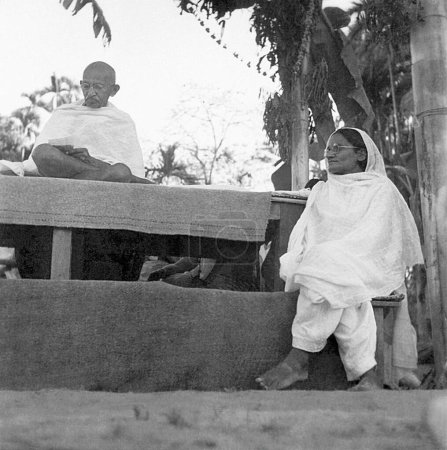 Téléchargez les photos : Mahatma Gandhi et Amtus Salam lors d'une réunion de prière dans la zone touchée par les émeutes du Noakhali Bengale oriental - en image libre de droit