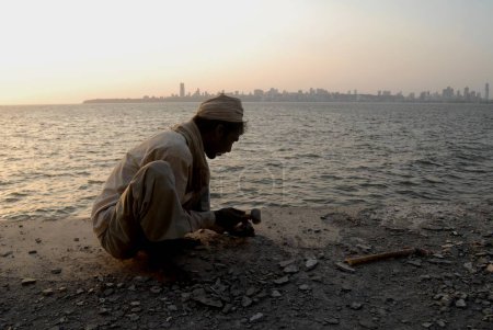 Foto de Un trabajador de la construcción trabaja durante la puesta del sol en Marine Drive; Bombay ahora Mumbai; Maharashtra; India - Imagen libre de derechos