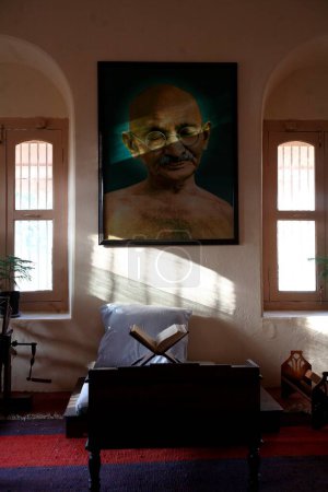 Photo for Mahatma Gandhi sitting place with his large photograph and his charkha at Satyagraha Ashram founded in 25 May 1915 at Kochrab.  Ahmedabad. Gujarat. India - Royalty Free Image