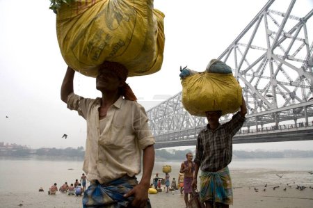 Téléchargez les photos : Les hommes portant la charge sur la tête Howrah pont sur HooApproximativement rivière en arrière-plan ; Calcutta maintenant Kolkata ; Bengale occidental ; Inde - en image libre de droit