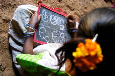Téléchargez les photos : Une fille tribale apprend les alphabets télougous à l'école dirigée par une ONG Organisation non gouvernementale dans un village de l'Andhra Pradesh, en Inde - en image libre de droit