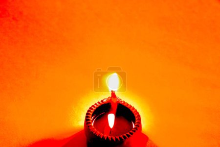 Schöne Kunst, eine einzige Diya-Ton-Öllampe als Lichtquelle auf orangefarbenem Hintergrund