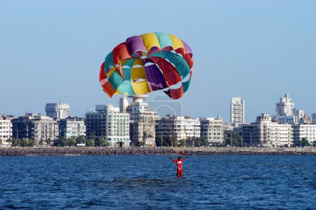 Téléchargez les photos : Parachutisme d'un homme avec parachute coloré sur Chowpatty, Marine Drive in, Mumbai Bombay, Maharashtra, Inde - en image libre de droit