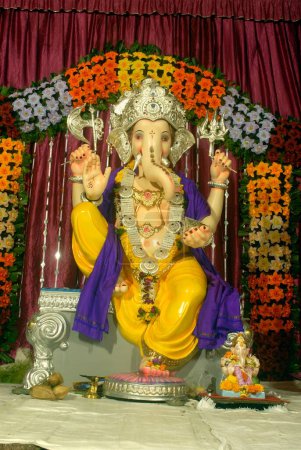 Téléchargez les photos : Idole colorée du Seigneur Ganesh avec une décoration simple de fleurs artificielles ; adoration pour la fête Ganapati ; dieu tête d'éléphant de l'hindouisme ; Pune ; Maharashtra ; Inde - en image libre de droit