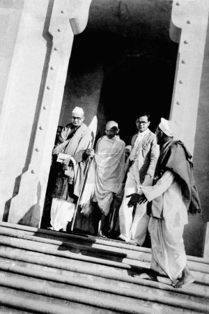 Foto de Mahadev Desai; Mahatma Gandhi y Satish Kalelkar hijo mayor de Kaka Kalelkar dejando un edificio en Varanasi; 1941; India - Imagen libre de derechos